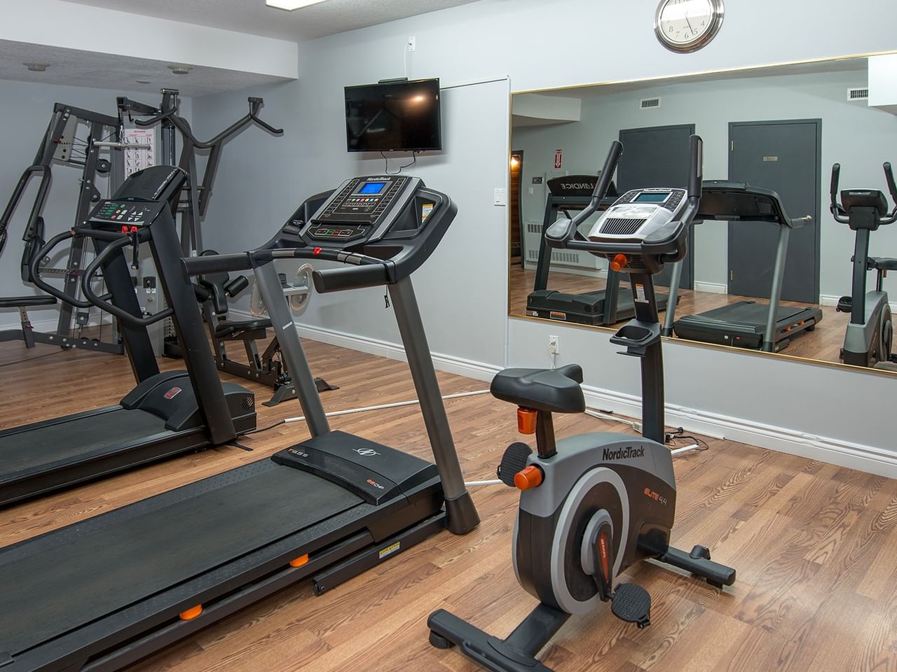 Two treadmills and one stationary bike in a gym room with large mirror reflecting the equipment.