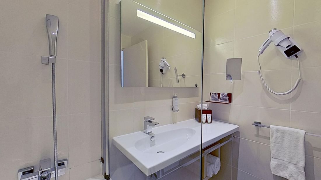 Bathroom with a shower, sink, mirror, towel rack, and a mounted hairdryer.