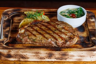 Bistec a la parrilla con aderezo de hierbas sobre un plato con papas asadas y un bol de espinacas en el Sunset Plaza Beach Resort, uno de los mejores hoteles con vistas a la playa en Puerto Vallarta