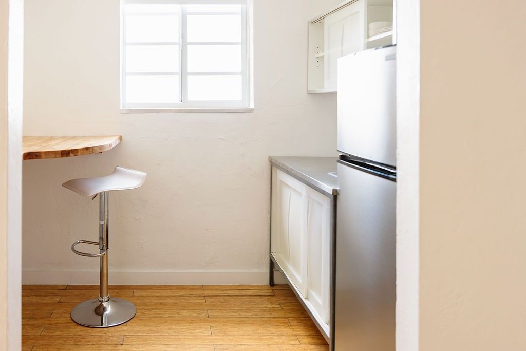 A small kitchenette with a white refrigerator, wooden counter, and a white stool.