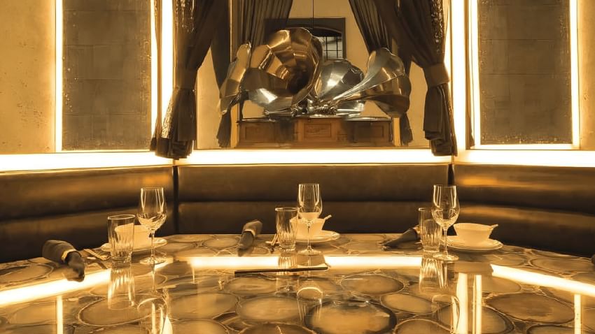 Mott 32 restaurant round table, set place settings, and modern decor with glowing lights and a large metal sculpture.