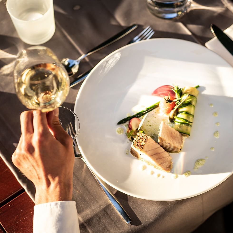 Mano con calice di vino bianco sopra un piatto elegantemente preparato