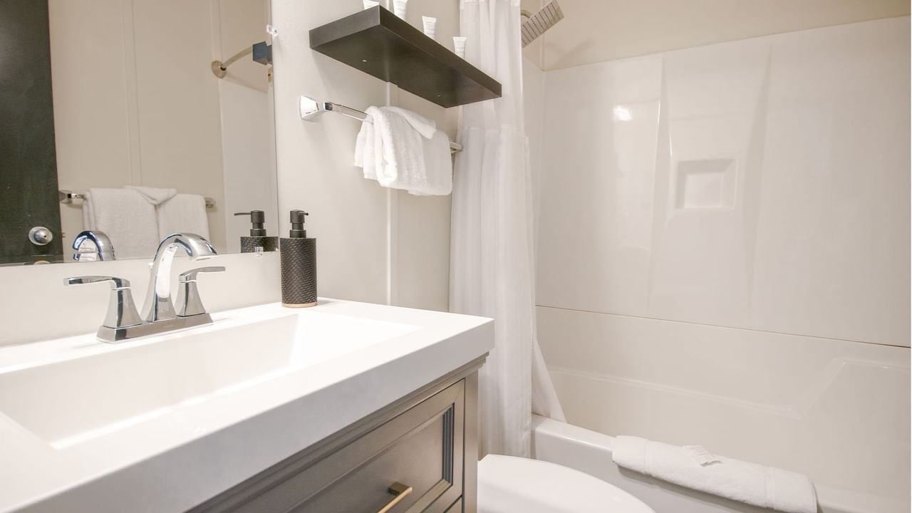 Hotel washroom with toilet, bathtub, sink, towels, and soap