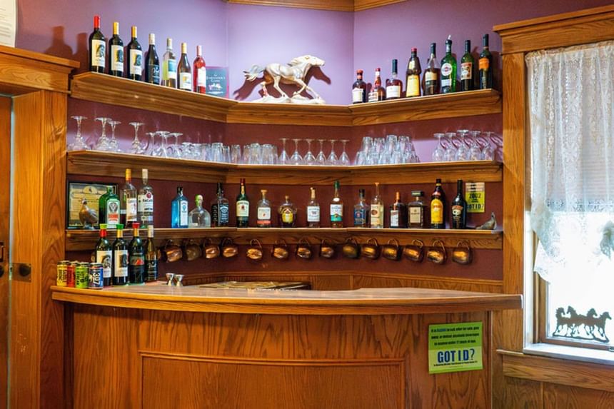 Fully stocked wooden bar at The Ranch at Ucross, with a selection of spirits, glassware, and western art