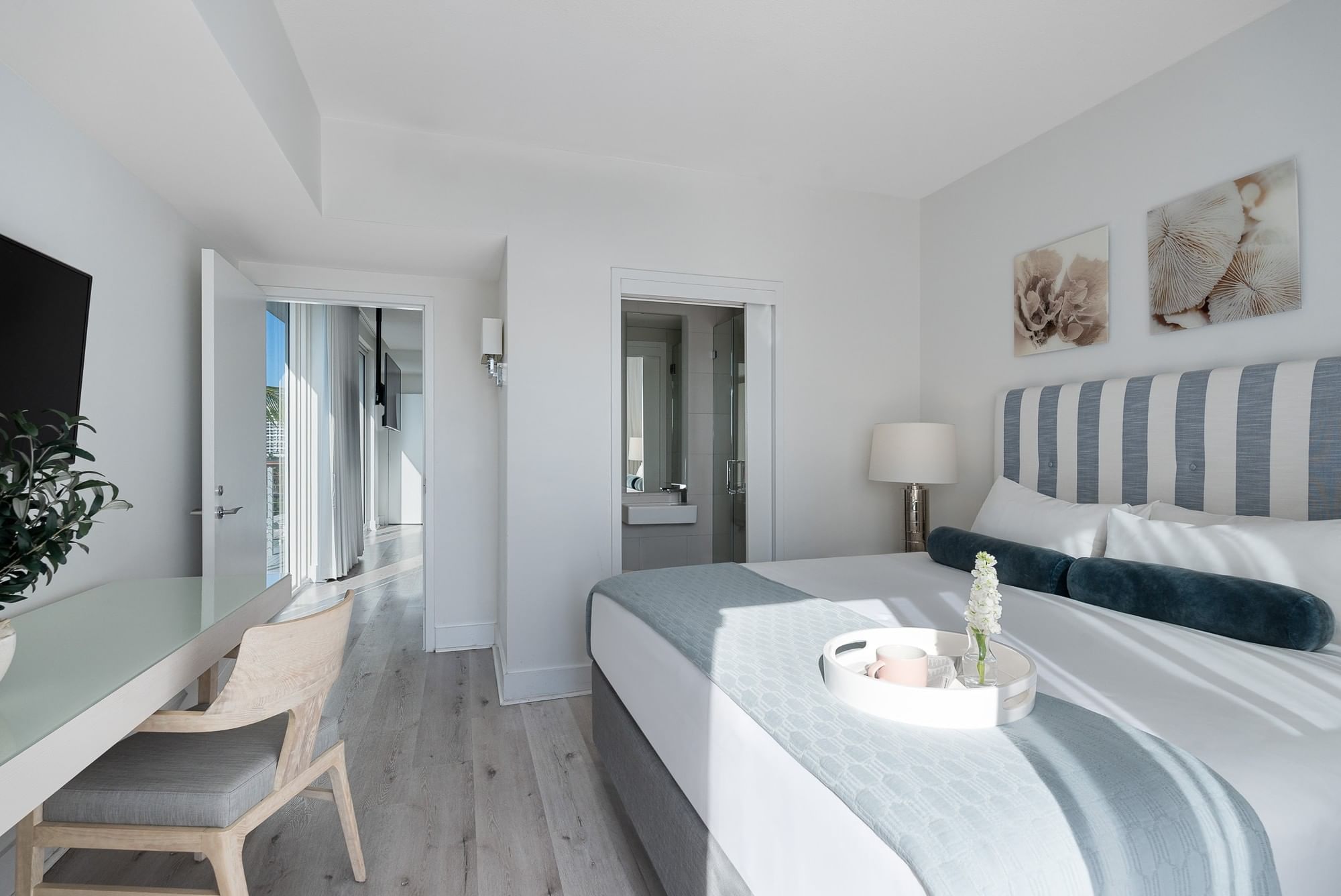 A bright and airy hotel room with a bed, desk, chair, and TV.