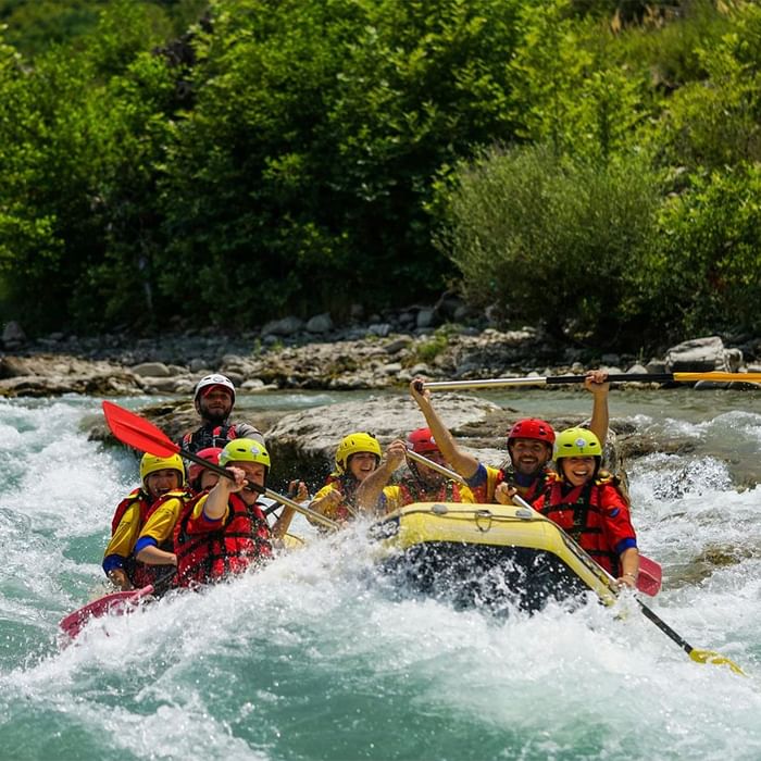 Gruppo di persone in un gommone giallo su un fiume, con rapide e vegetazione sullo sfondo.