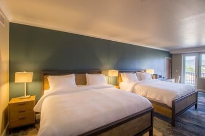 A spacious bedroom with two beds, a teal accent wall, and a large window in a room at The Stanley Hotel