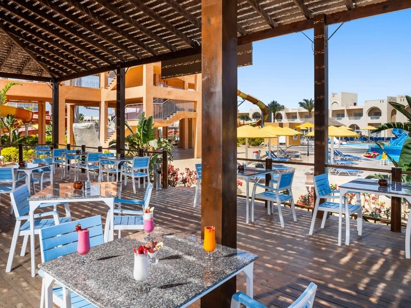 A resort restaurant patio with blue chairs, tables, and a scenic view of a pool and water slides.