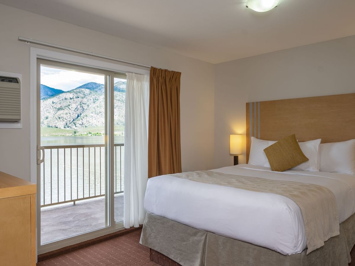 Bed in hotel room with balcony and view of lake