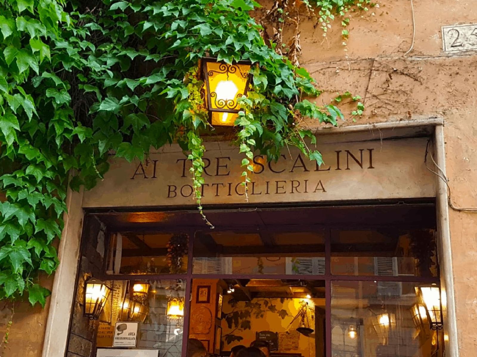 Facade of Ai Tre Scalini Bottiglieria, adorned with ivy and a warm lantern near The Glam Hotel