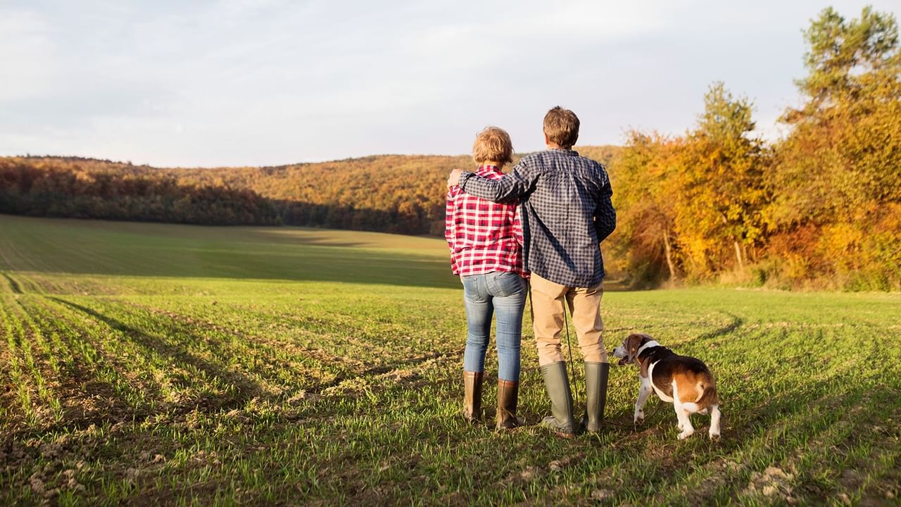 Couple standing together in a field, admiring the autumn landscape with a dog near Coast Penticton Hotel