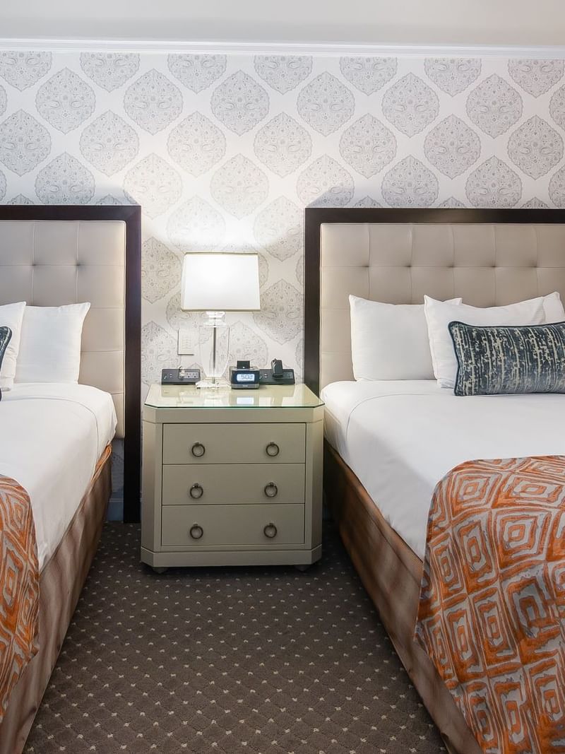 Two twin beds, sharing a bedside table with a lamp and clock in Premier Room 2 Double beds at Warwick New York