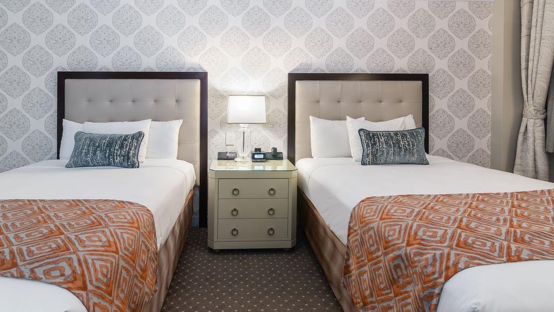 Two twin beds, sharing a bedside table with a lamp and clock in Premier Room 2 Double beds at Warwick New York