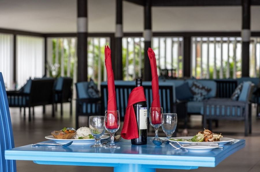 Table setting with wine, tall red napkins, and plates in Tambua Restaurant by blue sofas at Tambua Sands Beach Resort