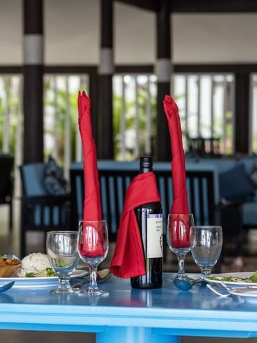 Table setting with wine, tall red napkins, and plates in Tambua Restaurant by blue sofas at Tambua Sands Beach Resort