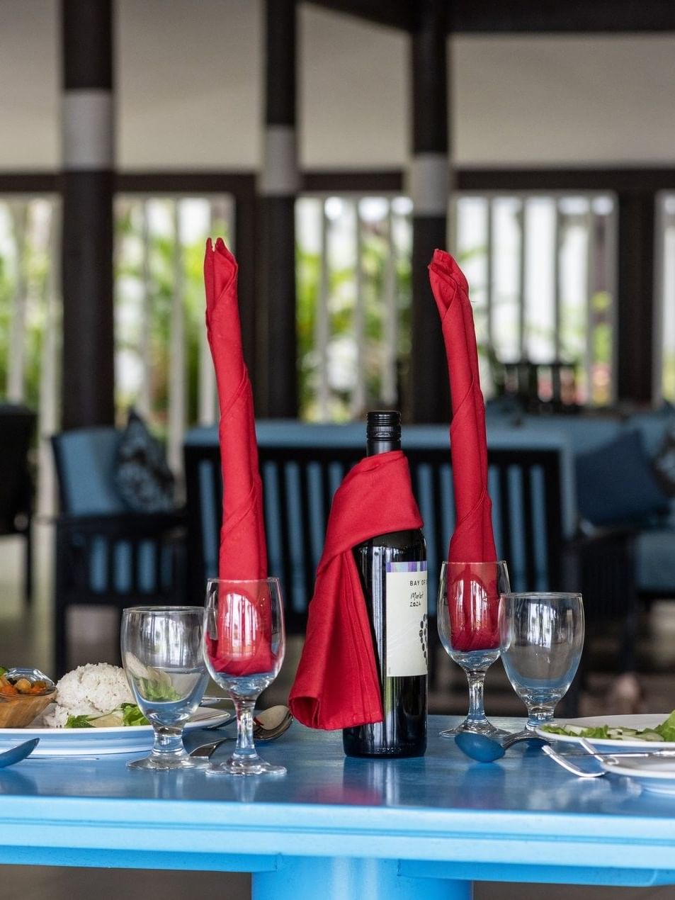 Table setting with wine, tall red napkins, and plates in Tambua Restaurant by blue sofas at Tambua Sands Beach Resort