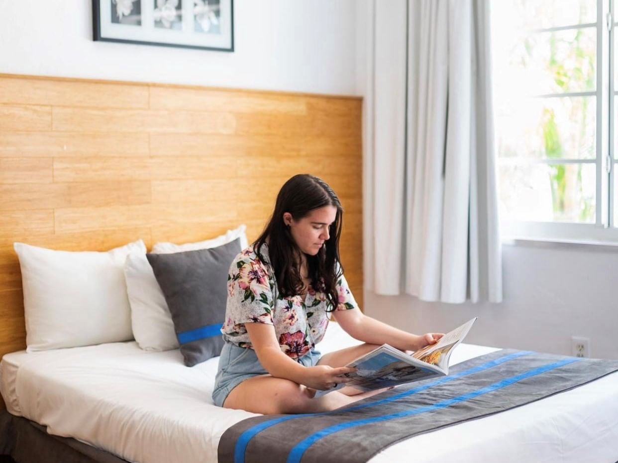 A girl seated on a bed & reading a magazine at Aqua Hotel