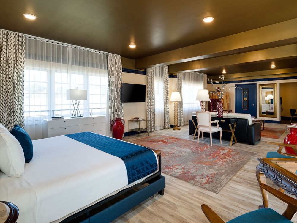 A wide view of a hotel room with a king bed, desk, seating area, and large window.