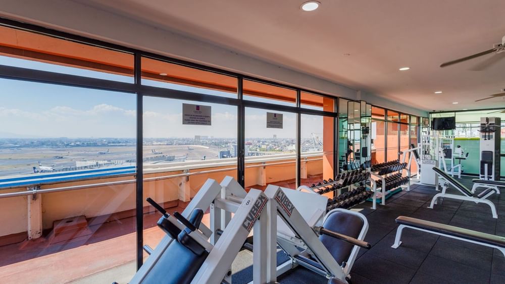 Gym with weight machines and dumbbells overlooking an airport runway at Camino Real Aeropuerto Mexico