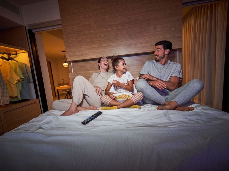 Family enjoying a movie on a bed at IOH Freestyle Hotels