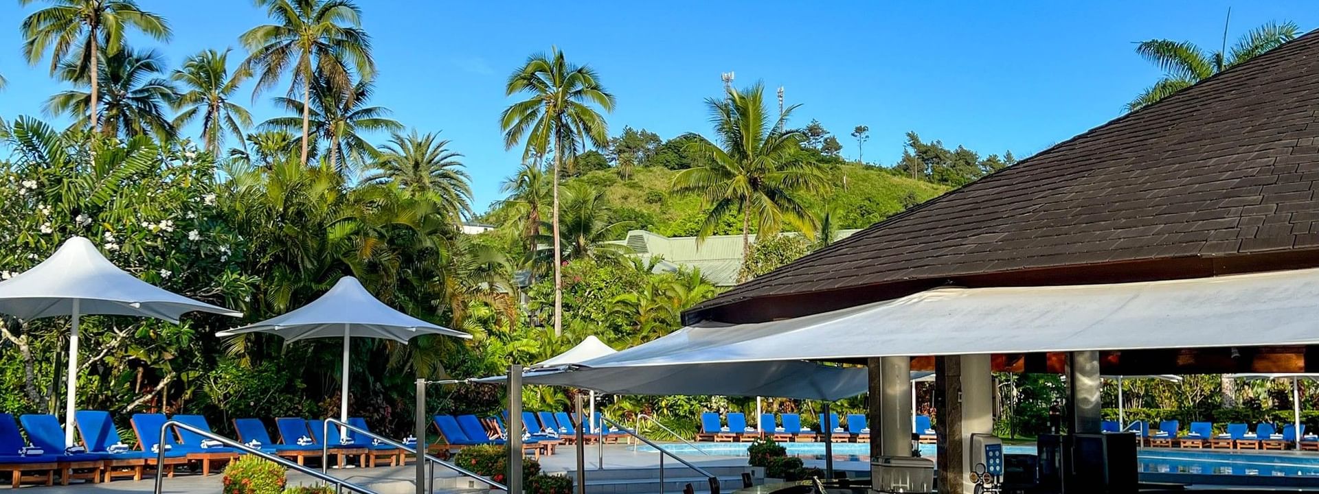 Vibrant poolside bar with wooden stools and blue lounge chairs under white canopies at The Naviti Resort in Korolevu