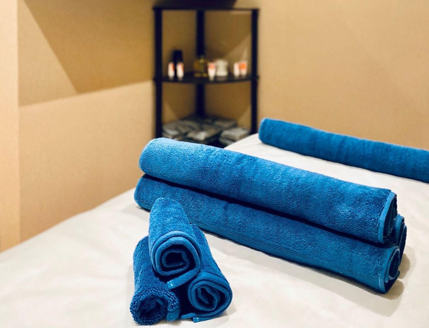 Gold Spa, featuring blue rolled towels on a bed near candles and oils by a corner shelf at Naviti By Warwick Dammam