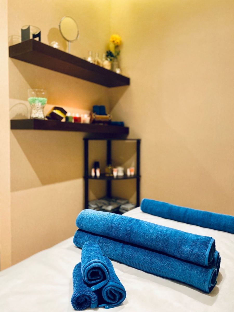 Gold Spa, featuring blue rolled towels on a bed near candles and oils by a corner shelf at Naviti By Warwick Dammam