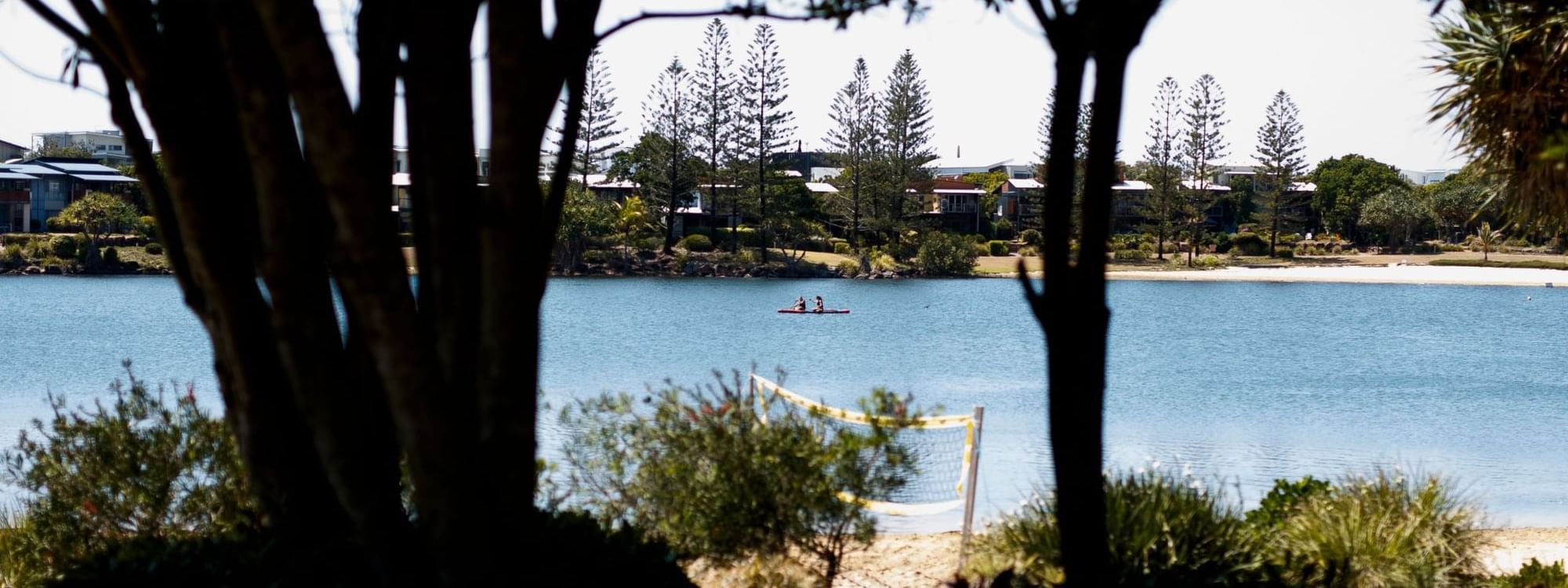 Two people paddling a kayak on calm blue water surrounded by trees and tall pines near Novotel Sunshine Coast Resort