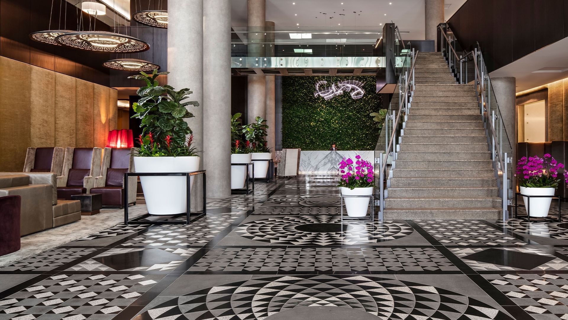 Grand lobby at Hotel X Toronto with geometric tiled floor and stone staircase beside green plant wall and orchids