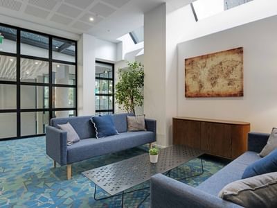 Modern lounge area with blue sofas, world map artwork, and skylights at UniLodge Auckland Central.