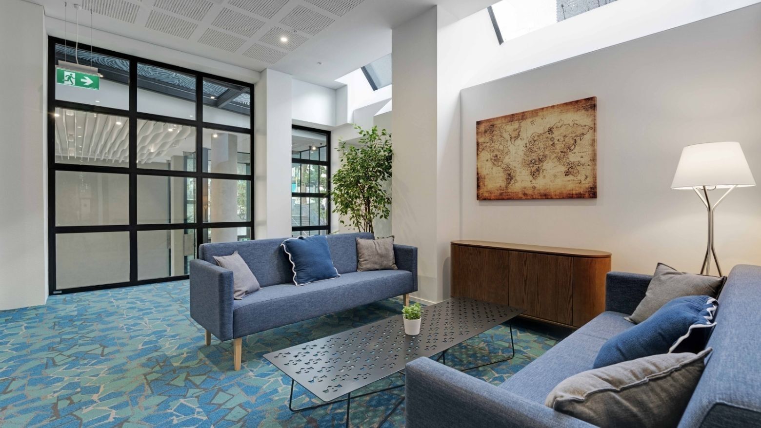 Modern lounge area with blue sofas, world map artwork, and skylights at UniLodge Auckland Central.