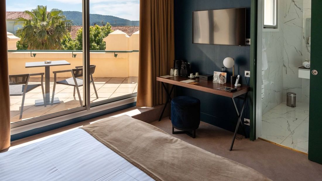 Chambre d'hôtel élégante avec vue sur la terrasse, un bureau et une douche vitrée.