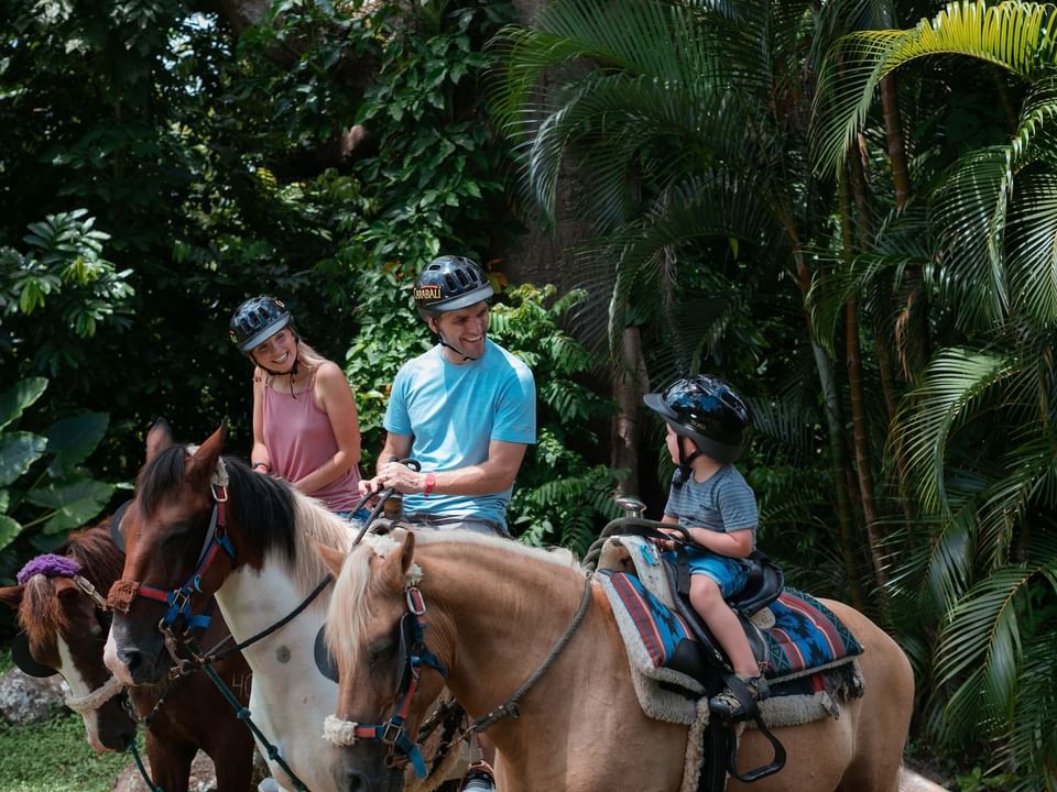 Una familia corriendo caballo explorando la selva en la Hacienda Carabali cerca de El Conquistador Resort