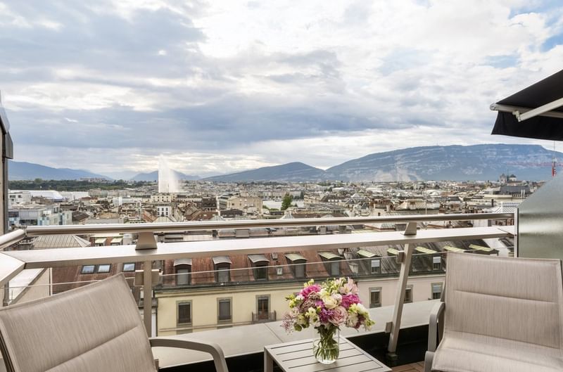 Vue panoramique depuis une terrasse avec chaises longues et bouquet de fleurs sur Genève et le Jet d'Eau au Warwick Geneva