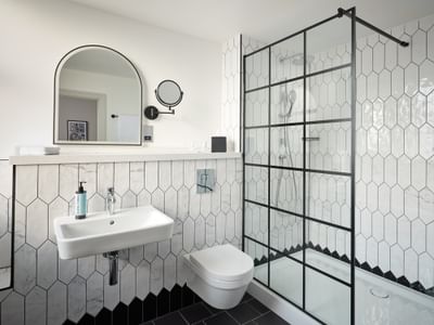 Contemporary suite bathroom at The Met Hotel Leeds, England, with toilet, sink, mirror, tiled walls, and a walk-in shower