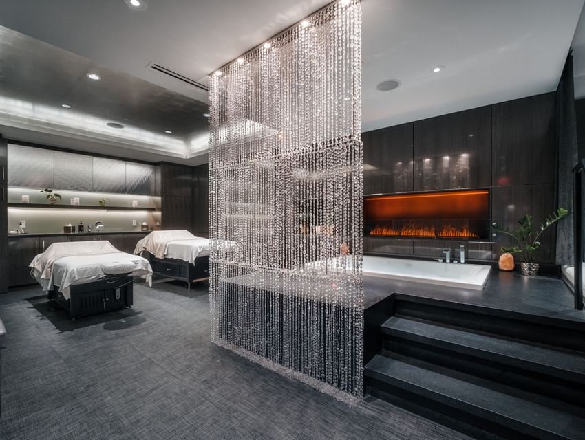 Elegant spa room with crystal curtain, two treatment beds, fireplace, and bathtub at Paradox Vancouver