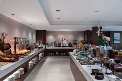 Wide buffet with pastries & cereals by wooden panels under bright spotlights in Rosa Restaurant at Warwick Al Taif Hotel
