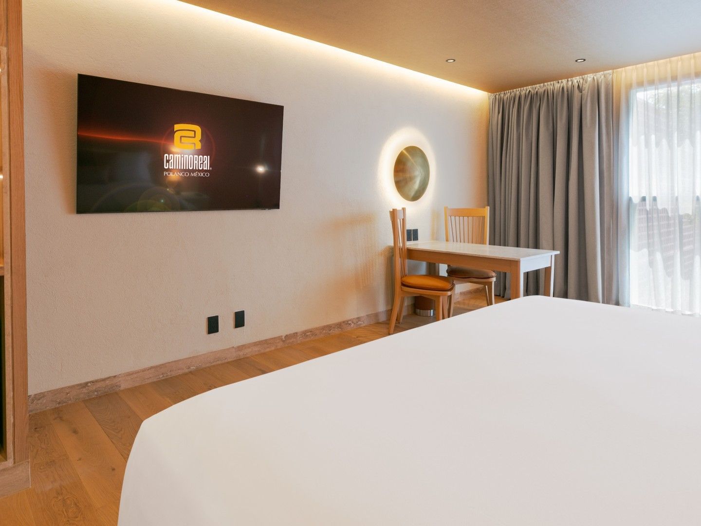 King Deluxe Plus room featuring a white bed, small dining table, and golden wall lamp at Camino Real Polanco Mexico