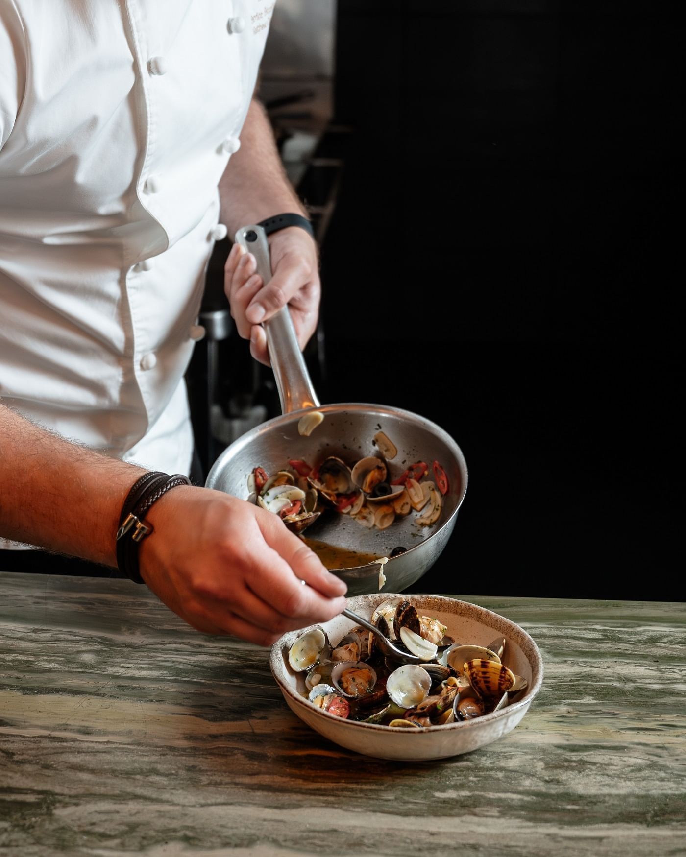 Close-up of a chef prepares mussels and shells in a bowl at The May Fair Hotel