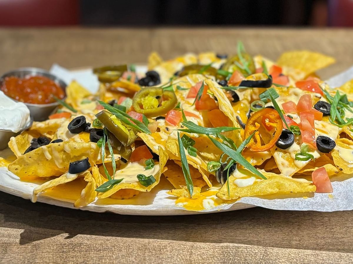 A plate of nachos topped with olives, tomatoes, jalapenos, and cheese, accompanied by sour cream and salsa.