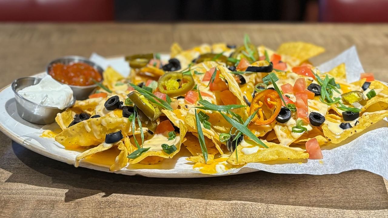 A plate of nachos topped with olives, tomatoes, jalapenos, and cheese, accompanied by sour cream and salsa.