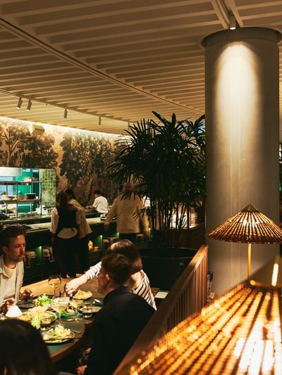 People dining at tables in a restaurant with large columns and ceiling lamps.