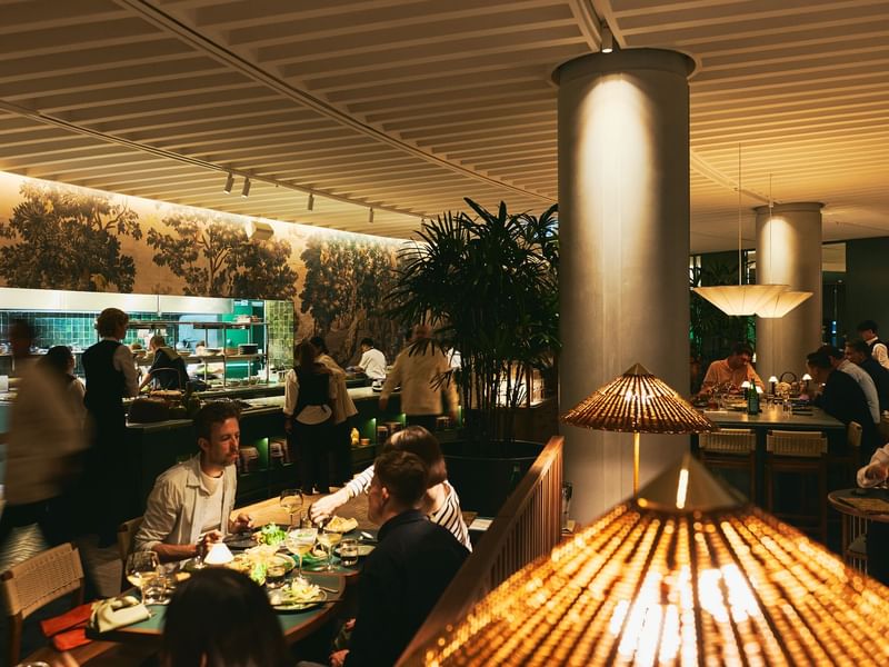 People dining at tables in a restaurant with large columns and ceiling lamps.