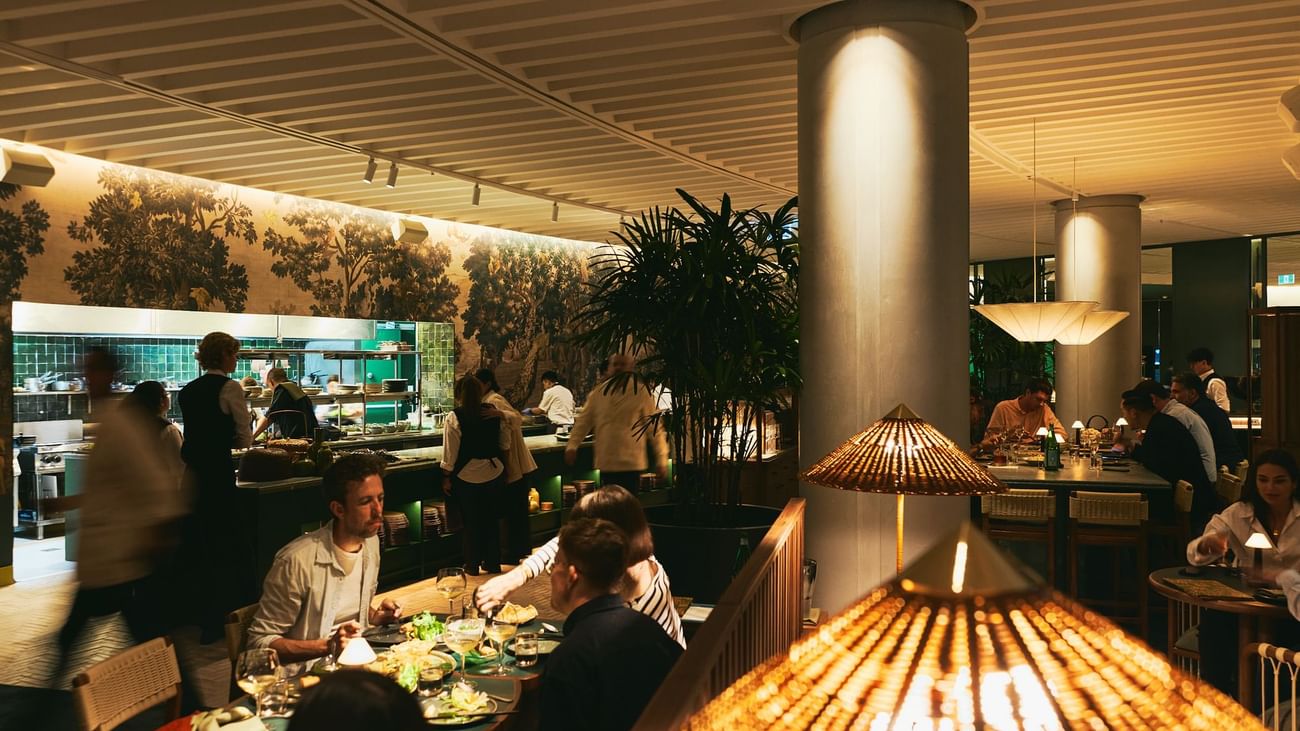 People dining at tables in a restaurant with large columns and ceiling lamps.