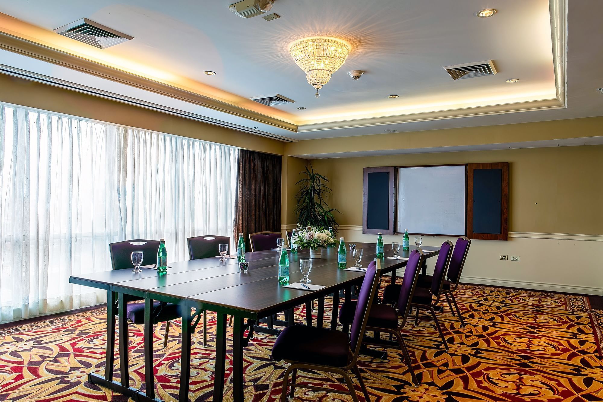 A meeting room with a long table, purple chairs, a whiteboard, and a chandelier.