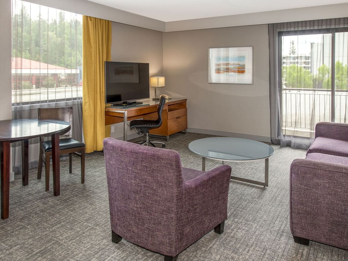 A hotel suite with a living area with TV, a desk and a balcony.