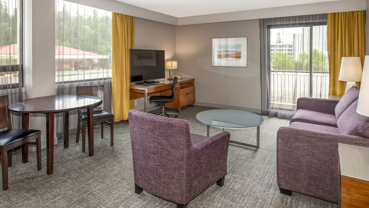 A hotel suite with a living area with TV, a desk and a balcony.