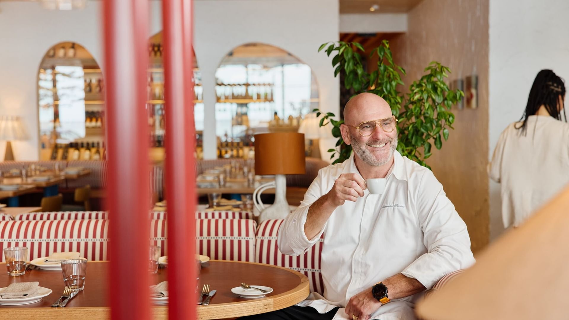 Bald chef in a white jacket drinks espresso on a striped banquette at Elysium Manly, fine for 5-star hotels, Manly