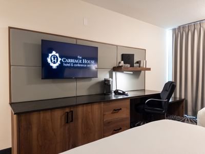 Hotel room with a desk, chair, television, and a bed at Carriage House Hotel & Conference Centre.