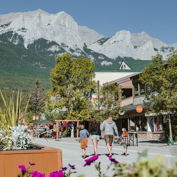 Family strolling through downtown Canmore with mountain views and colourful flowers during shoulder season.